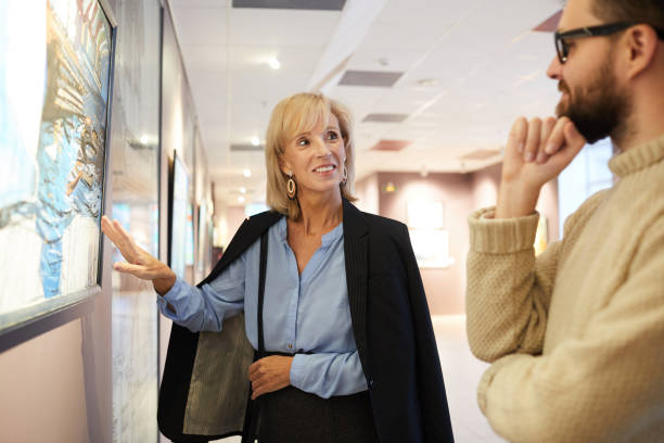 smiling woman pointing at painting in art gallery - group of people art museum clothing lifestyles imagens e fotografias de stock