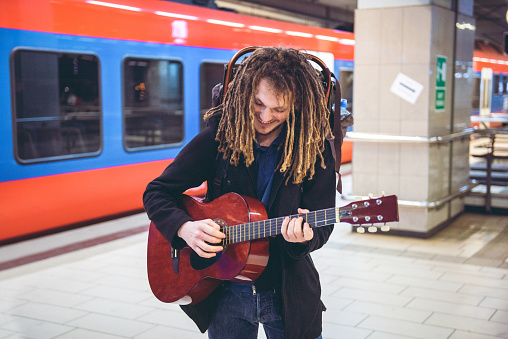 Young man playing acoustic guitar at the train station while waiting for his train