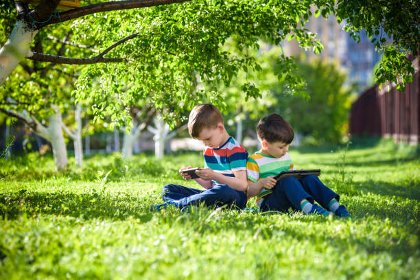 istock Two brother kid is lying on the grass with tablet. 1206878282