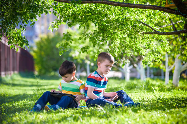 istock Two brother kid is lying on the grass with tablet. 1206878709