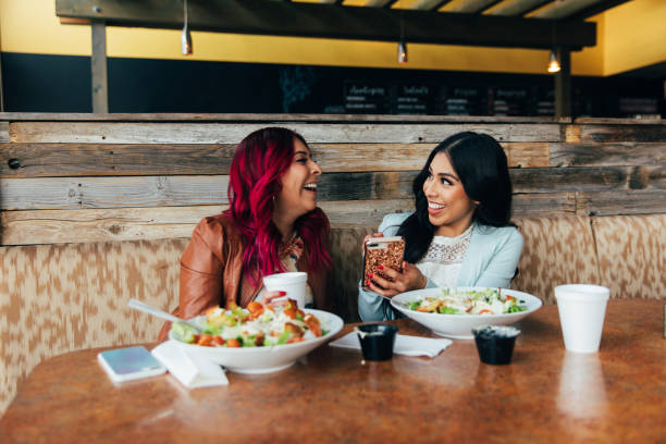 Young Hispanic Millennial women and sisters are on a phone while at a restaurant for lunch. She is sitting at a table with her salad smiling while she is interacting online and looking at her bank account. Image taken in Utah, USA.