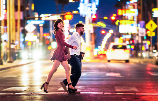 A couple rushing across the street in Las Vegas, Nevada, with bright city lights in the background.
