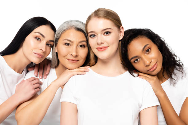 cheerful multicultural women in white t-shirts looking at camera isolated on white cheerful multicultural women in white t-shirts looking at camera isolated on white group of women all ages stock pictures, royalty-free photos & images
