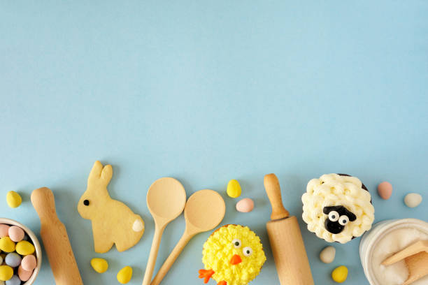 Easter or spring baking scene of various sweets and cookies, top view bottom border over a blue background