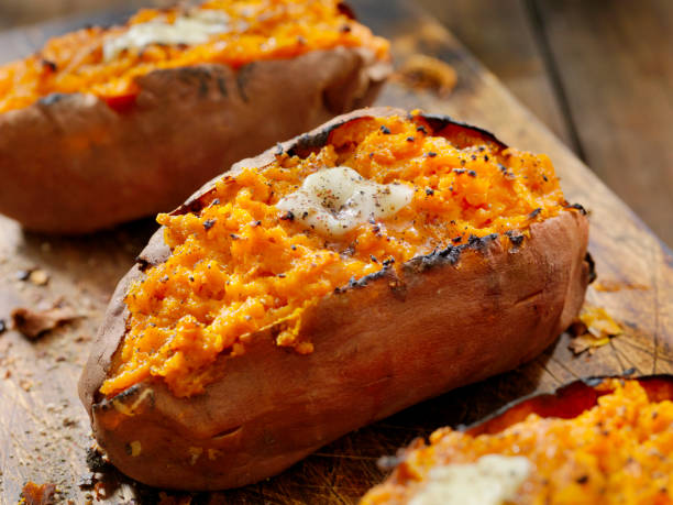 tweemaal gebakken, gevulde zoete aardappelen met smeltende boter en gebarsten peper - gebakken in de oven stockfoto's en -beelden