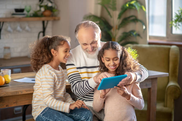 istock Grey-haired bearded man and his granddaughters watching a video on tablet 1206891298