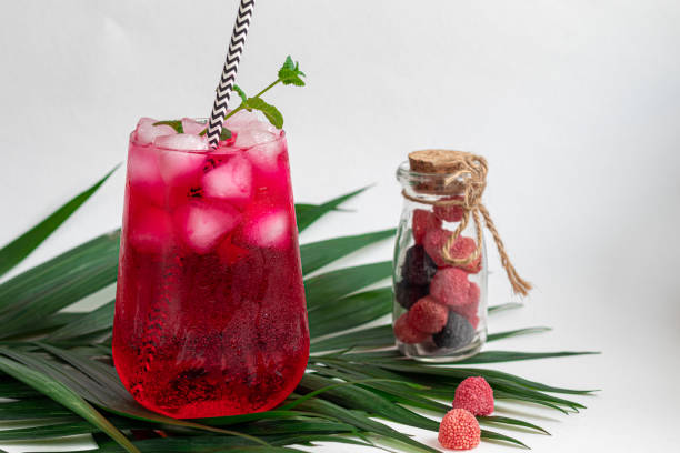 istock Raspberry-barberry drink in a transparent glass with ice. Added palm branches and raspberries. White background. 1206891662