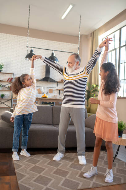 istock Bearded grey-haired man dancing with his granddaughters and feeling great 1206891795