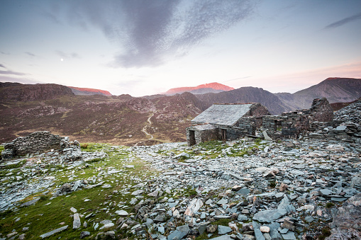 Dubs Hut, an abandoned old bothy and slate mine workings on Fleetwith Pike looking towards Haystacks in early summer at sunrise and moonset in the English Lake District.