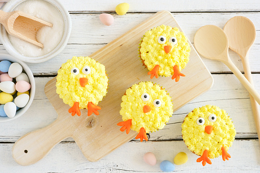Cute Easter chick cupcakes. Above view table scene with a white wood background.
