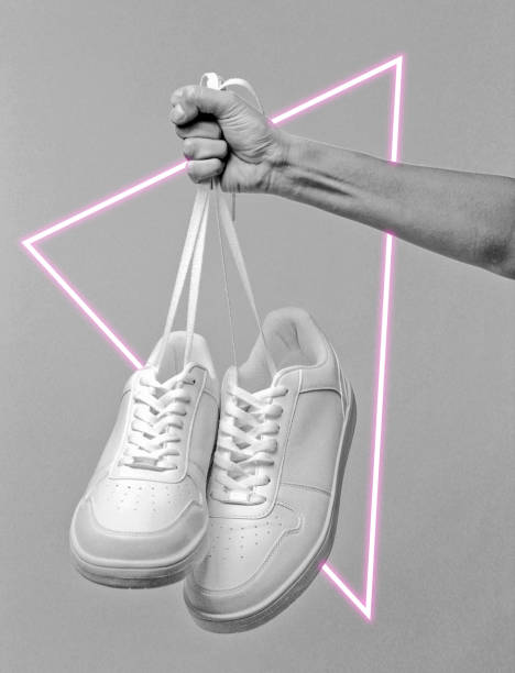 istock Hand holds sneakers by the laces. 80's synth wave and retrowave glowing triangle futuristic aesthetics. Old fashioned abstraction concept 1206894505