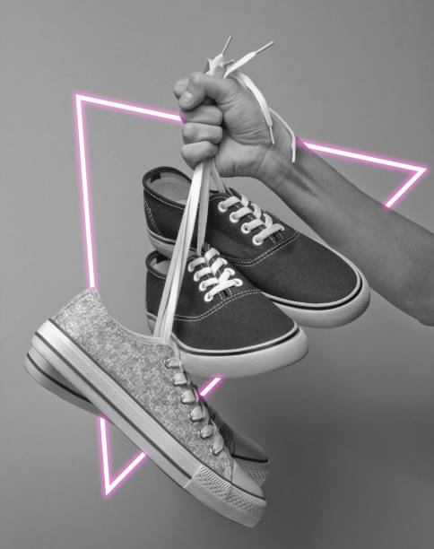 istock Hand holds sneakers by the laces. 80's synth wave and retrowave glowing triangle futuristic aesthetics. Old fashioned abstraction concept 1206894553
