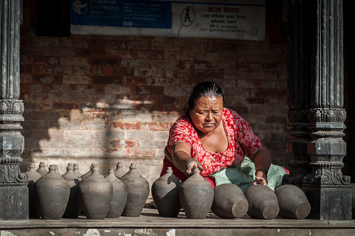 Nepalese woman making pottery in Pottery square, a public square full of pottery wheels and rows of clay pots which are made by old fashioned way drying in the sun - Bhaktapur, Nepal