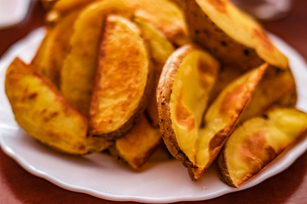 Close-Up Of Prepared Potatoes In white dish.Fried Potato Wedges on white dish a wood table.Directly Above Shot Of Fried Potatoes In Bowl.Fast food.Golden yummy Fried Potato Wedges,top view, lifestyle primer plano de patatas preparadas en plato blanco. cuñas de patata fritas en plato blanco una mesa de madera. directamente por encima de shot of fried potatoes in bowl.fast food. cuñas de patata fritas doradas, vista superior, estilo de vida