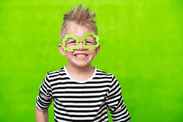Portrait Little smiling caucasian boy in mask of leprechaun shamrock clover glasses for irish St. Patrick's Day on green studio background. Copyspace portrait little smiling caucasian boy in mask of leprechaun shamrock clover glasses for irish St. Patrick's Day on green studio background. Copyspace. good luck charm photos stock pictures, royalty-free photos & images