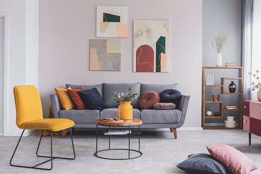 Real photo of a yellow chair and gray couch with pillows in a modern living room interior