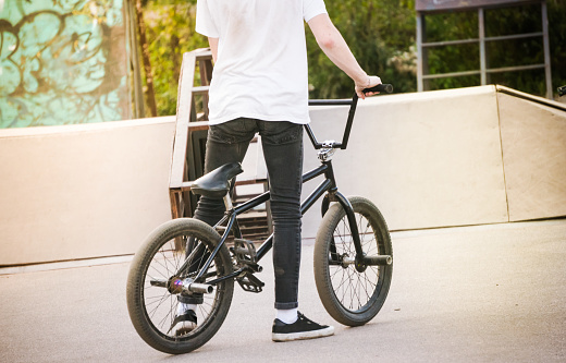 Caucasian teenage boy standing by bmx bike at skatepark