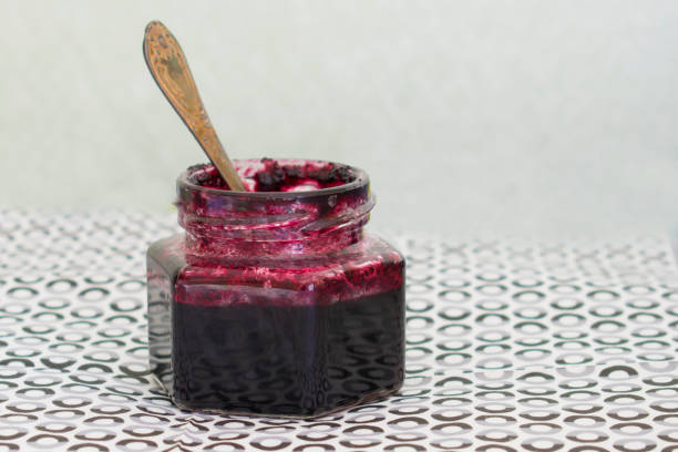 A jar with a spoon on a table with blueberry jam. Homemade vitamin preserves from berries.