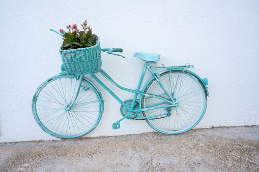 Turquoise vintage bicycle with flowers in the basket on Mediterranean white wall