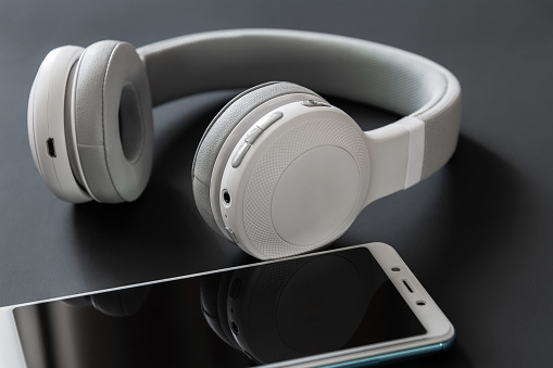Wireless headphones and smartphone on the dark background. Closeup, selective focus