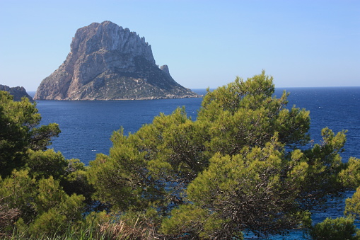 The island of Es Vedra between the blue sky and the blue sea of the Ibizan coasts in front of the Cala D'Hort beach in the Balearic Islands in spain