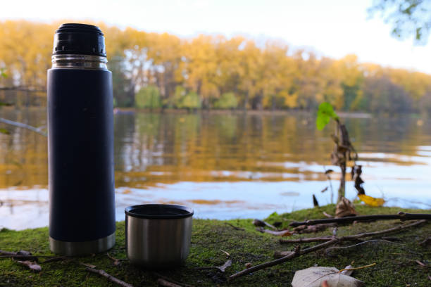 istock Thermos Vacuum flask in forest and lake. Close up 1206911803