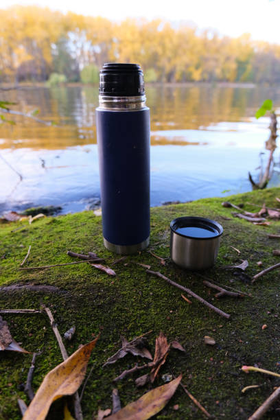 istock Thermos Vacuum flask in forest and lake. Close up 1206911959