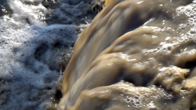A rapid stream of dirty brown water flows into the river. Environmental pollution. Concept. Close-up. 4K