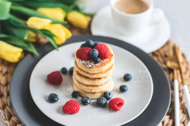 Photo of Cottage cheese pancakes with berries, healthy breakfast, yellows tulips, spring, woman's day
