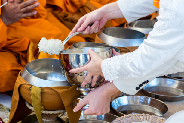 Offer food to monk. Groom give alms food to a Buddhist monk in traditional thai wedding ceremony. Hand while put food offerings in a Buddhist monk's alms bowl.Buddhists offer food in bowls. ofrezca comida al monje. el novio da comida a la limosna a un monje budista en la ceremonia de boda tradicional tailandesa. mano mientras pone ofrendas de comida en el cuenco de limosna de un monje budista. los budistas ofrecen comida en cuencos.