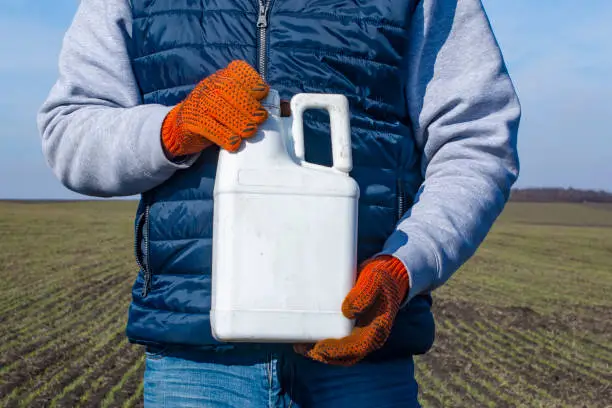 Protection of crops from pests and diseases. Bottle with a pesticide in the hand of an agronomist.