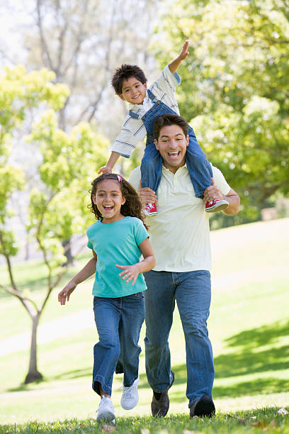 отец и дети, бег на открытом воздухе улыбается - family with two children family park child стоковые фото и изображения