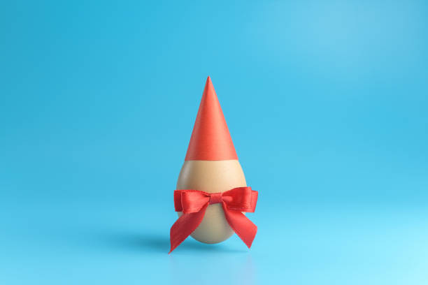 istock One brown egg with a red ribbon bow in a red festive cap on a blue background. 1206927814