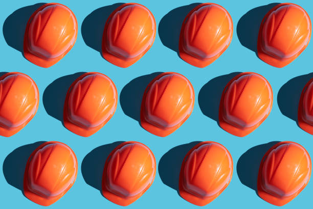 orange safety helmet rows on a blue background with hard shadows. looking from above.industrial pattern backdrop.