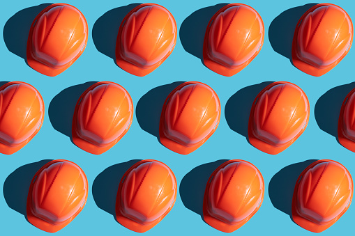 orange safety helmet rows on a blue background with hard shadows. looking from above.industrial pattern backdrop.