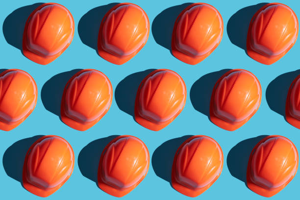 orange safety helmet rows on a blue background with hard shadows. looking from above.industrial pattern backdrop. - protective workwear hat violence construction imagens e fotografias de stock