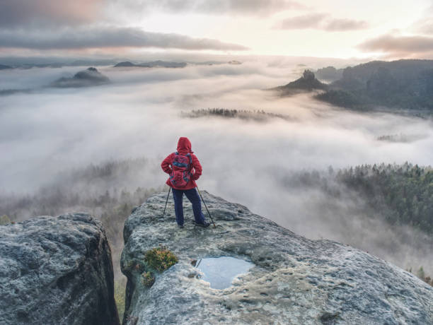 Photo of Backpacker stay on wet rock. Misty daybreak in rocky mountains