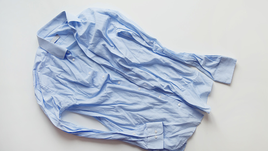 Blue cotton wrinkled and rumpled shirt on white. Washed shirt after tumble dryer.