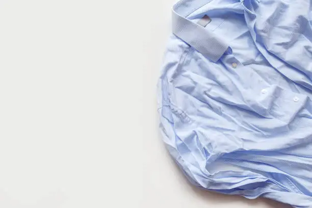 Photo of Blue cotton wrinkled and rumpled shirt on white. Washed shirt after tumble dryer