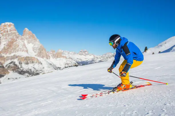 Male skier in blue and yellow clothes on slope with mountains in the background at Cortina d'Ampezzo Faloria skiing resort area Dolomiti Italy