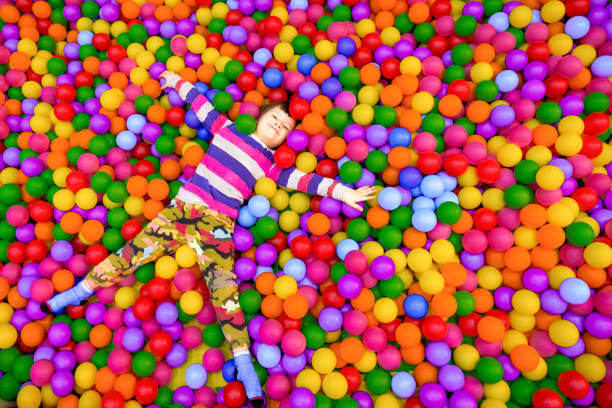 Emotional cheerful little child having fun in entertainment game center. Happy baby boy lying in pool filled with lot of colorful foam rubber balls in children's entertainment complex. Copy space Little boy playing in dry pool with plastic balls in the nursery. Close-up leisure activities indoors. Positive emotions background. School holidays. Copy space home cinema system stock pictures, royalty-free photos & images