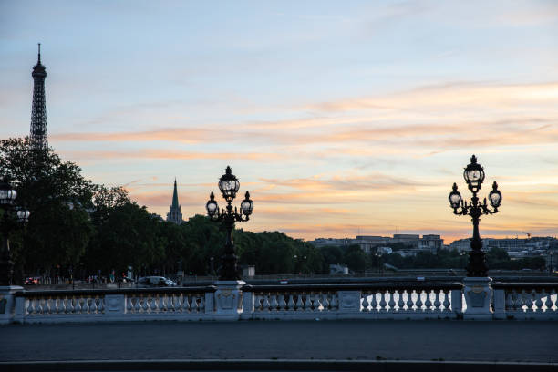 Beautiful sunset in Paris on a historical bridge. Eiffel Tower poking out from Trees, unique lamp posts along river Seine.