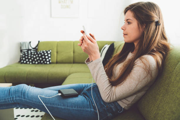 istock Woman sitting on the couch using her phone while charging it on power bank 1206954992