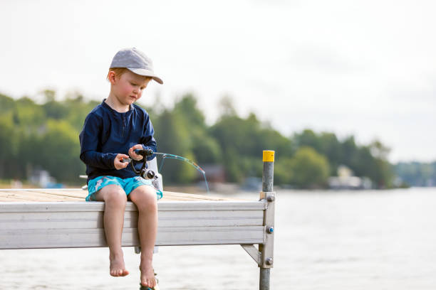 Lovely asian child sitting on bamboo litter. Happy girl pulling rod in her hands while fishing against landscape of lake. Concept of connecting children with nature. Travel on vacation.