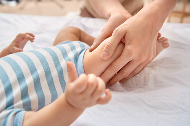 cura del bambino. giovane madre che fa massaggio pediatrico massaggiando le gambe del figlio piccolo sdraiato sul letto da vicino - alternative therapy foto e immagini stock