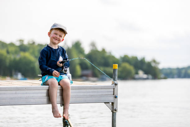 Photo of a young boy holding a fishing pole while sitting on a dock near a lake