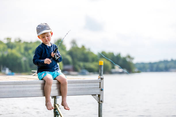 A little redhead boy is learning to fish in summer. It is his first time and he is very concentrated on the task. Taken at Lac St-Joseph, Quebec, Canada