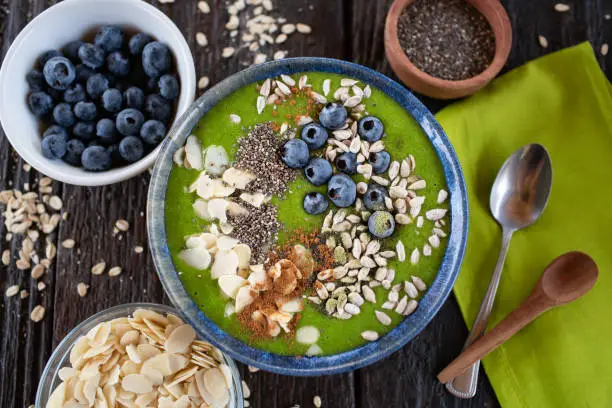 Green smoothie bowl with almonds, blueberries, chia and sunflower seeds, healthy superfood breakfast concept