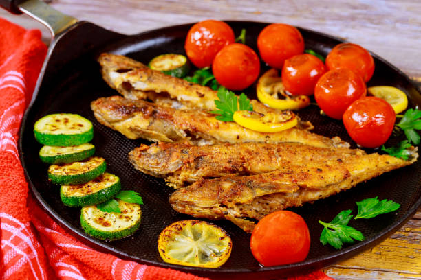 istock Fried whole fish with vegetable on black skillet. 1206976107
