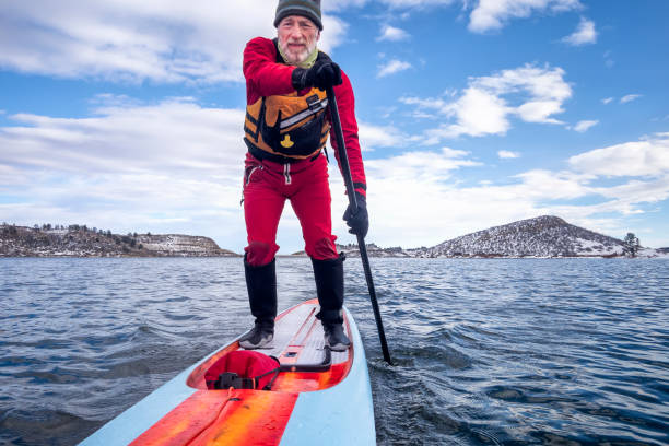 aktiver senior paddelt im winter stand up paddlenboard - fort collins reservoir lake water stock-fotos und bilder